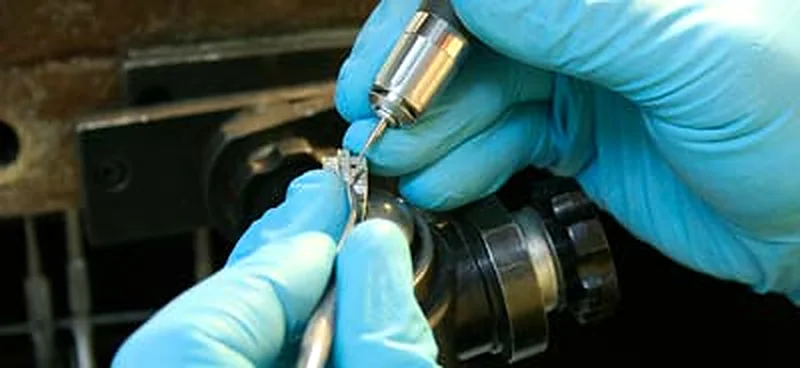 A gloved hand working a small piece under a jeweller's flex-shaft tool